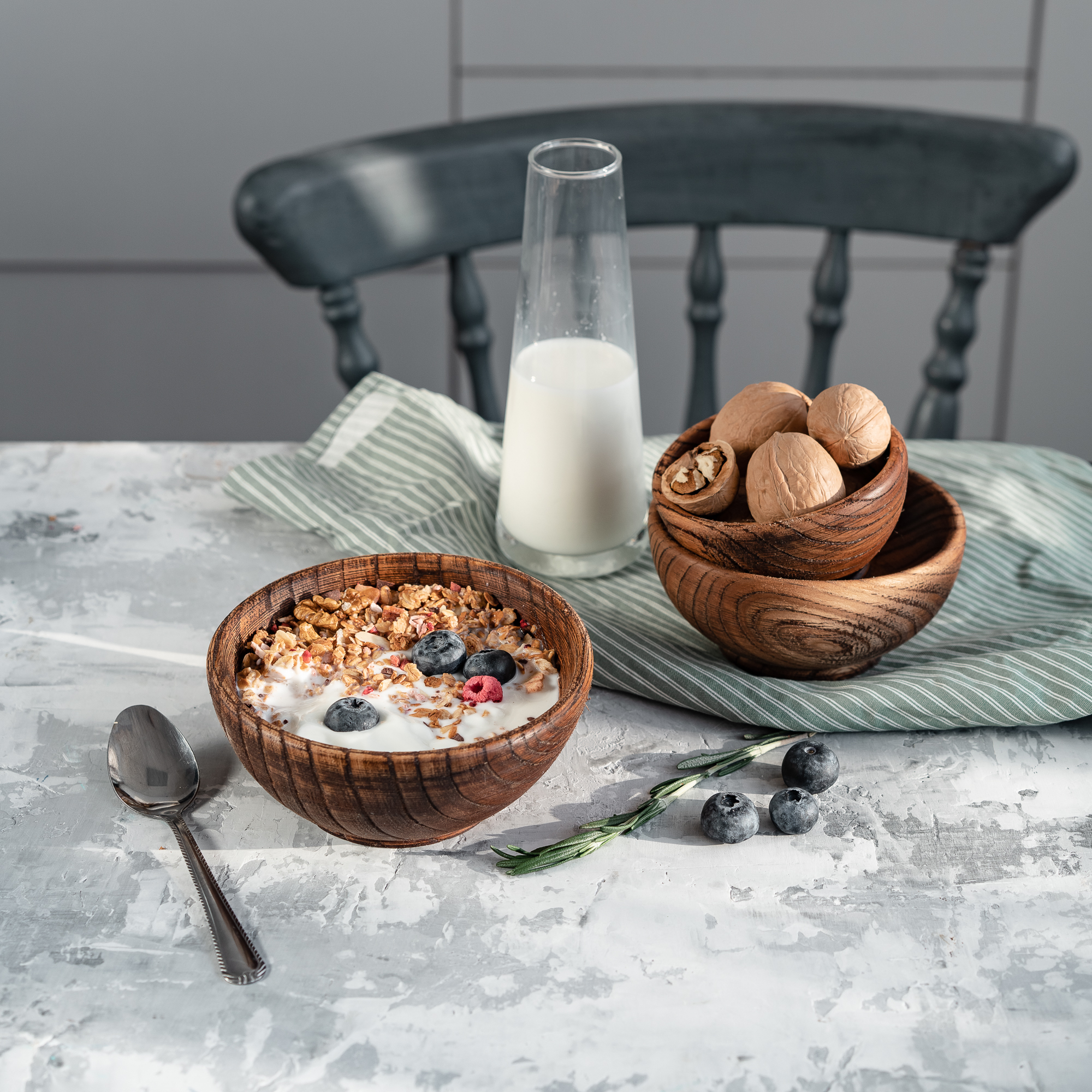 Wooden kitchen table with natural linen, a small bowl of oats, and scattered mixed berries in soft daylight
